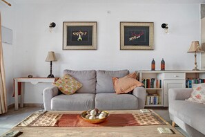 Een woonkamer met een grijze bank, een bijzettafel met decoratieve objecten, een boekenkast en twee ingelijste kunstwerken aan de muur.