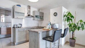 Una cucina moderna con isola centrale, sgabelli da bar, una pianta in vaso e un orologio a parete.