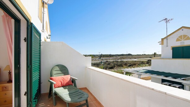 A balcony with a chair, a table, and a view of a distant landscape.