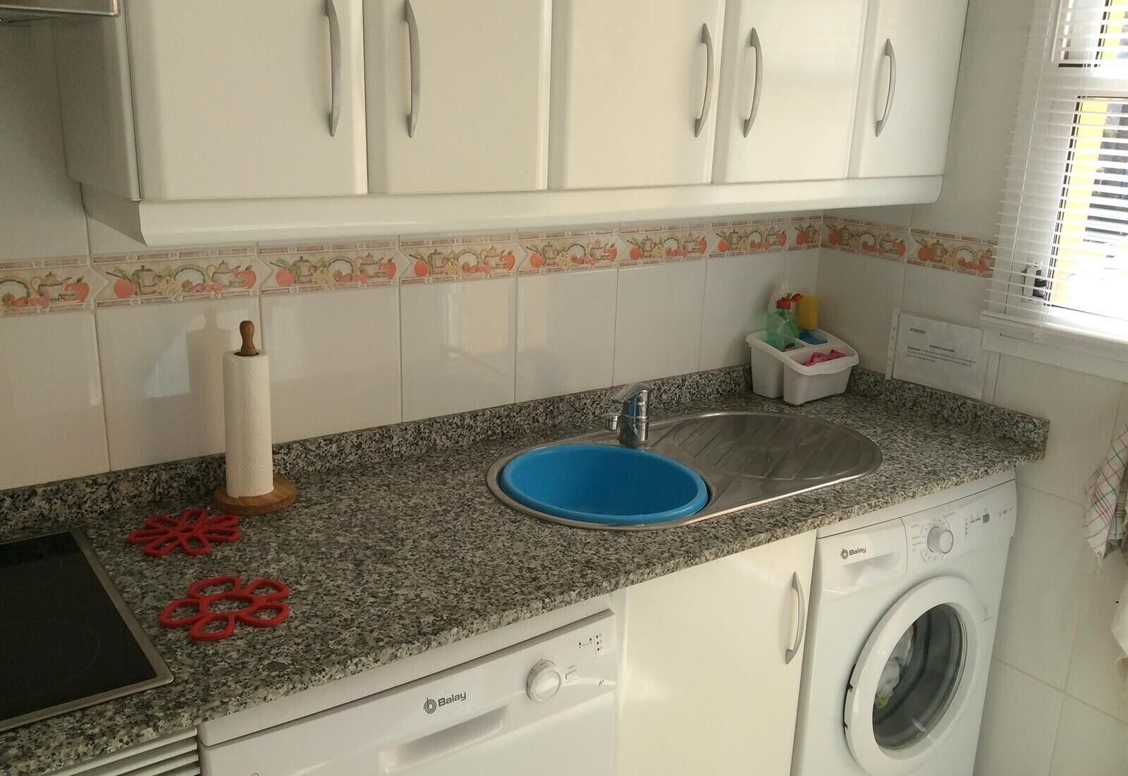 Eine Küche mit weißen Schränken, einer Granit-Arbeitsplatte, einem blauen Spülbecken, einer Waschmaschine und einer Küchenpapierrolle.