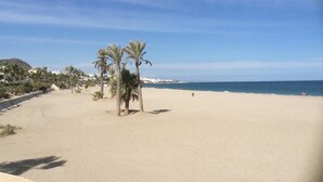 Una playa con palmeras, cielo despejado y una costa distante.