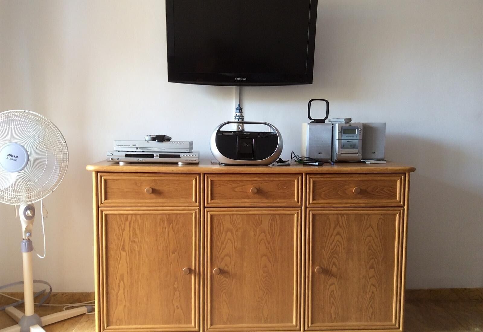 Un mueble de madera con un televisor de pantalla plana, una radio y un pequeño dispositivo encima.