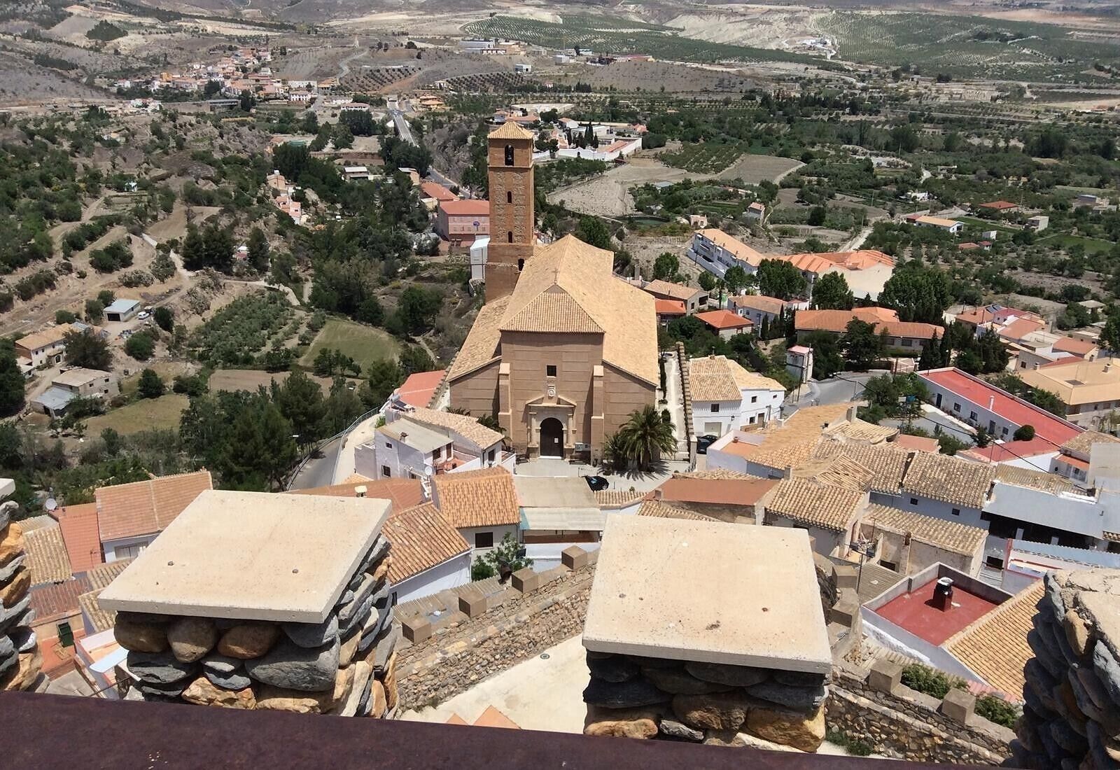 A town with a prominent church featuring a bell tower, surrounded by residential buildings with red-tiled roofs.