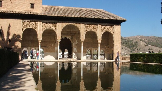 Un edificio histórico con paseos arqueados y una piscina reflectante.