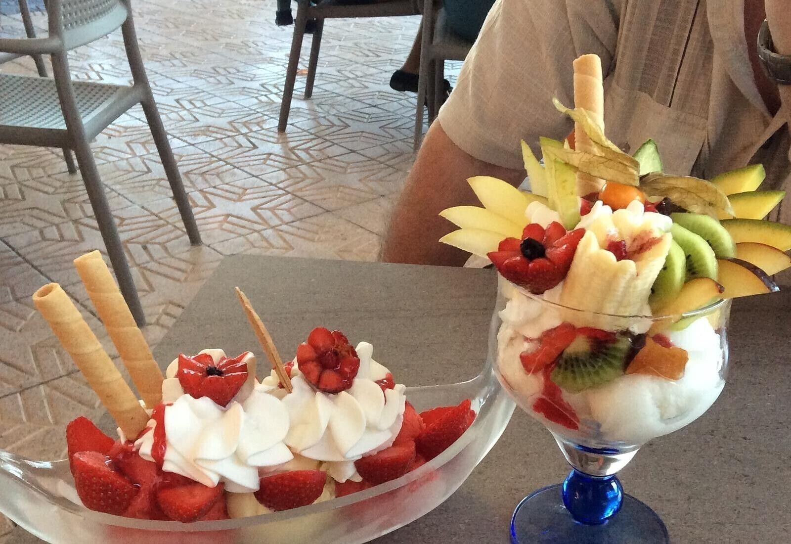 Two dessert bowls with fruits and whipped cream, placed on a table.