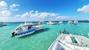Una marina con diverse imbarcazioni ormeggiate, acqua turchese cristallina e un cielo azzurro intenso.