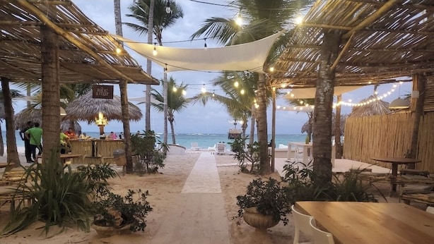 Un ristorante sulla spiaggia con tetti di paglia, luci a catena e posti a sedere all'aperto.