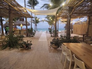 A beachside restaurant with thatched roofs, string lights, and outdoor seating. - Punta Cana Ocean View Penthouse - Private Rooftop - 1 min to the Beach - 3BR (bavaro)