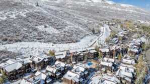 Une ville de montagne enneigée, avec ses bâtiments traditionnels en bois, une piste de ski et un ciel bleu azur.
