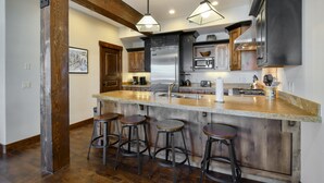 Une cuisine dotée d’un îlot central, de tabourets de bar, d’appareils électroménagers en acier inoxydable et de poutres en bois.