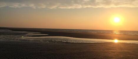 Une plage où le soleil se couche à l’horizon.