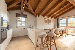 Una cocina moderna con vigas de madera, una isla grande, taburetes de bar y un comedor con vistas.