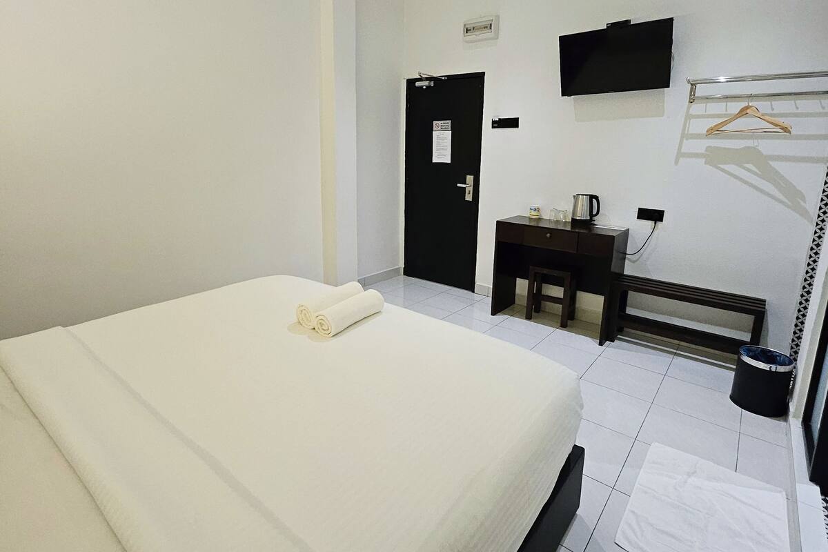 Ein Hotelzimmer mit einem großen Bett, einem Schreibtisch, einem Fernseher und einem Kleiderständer.