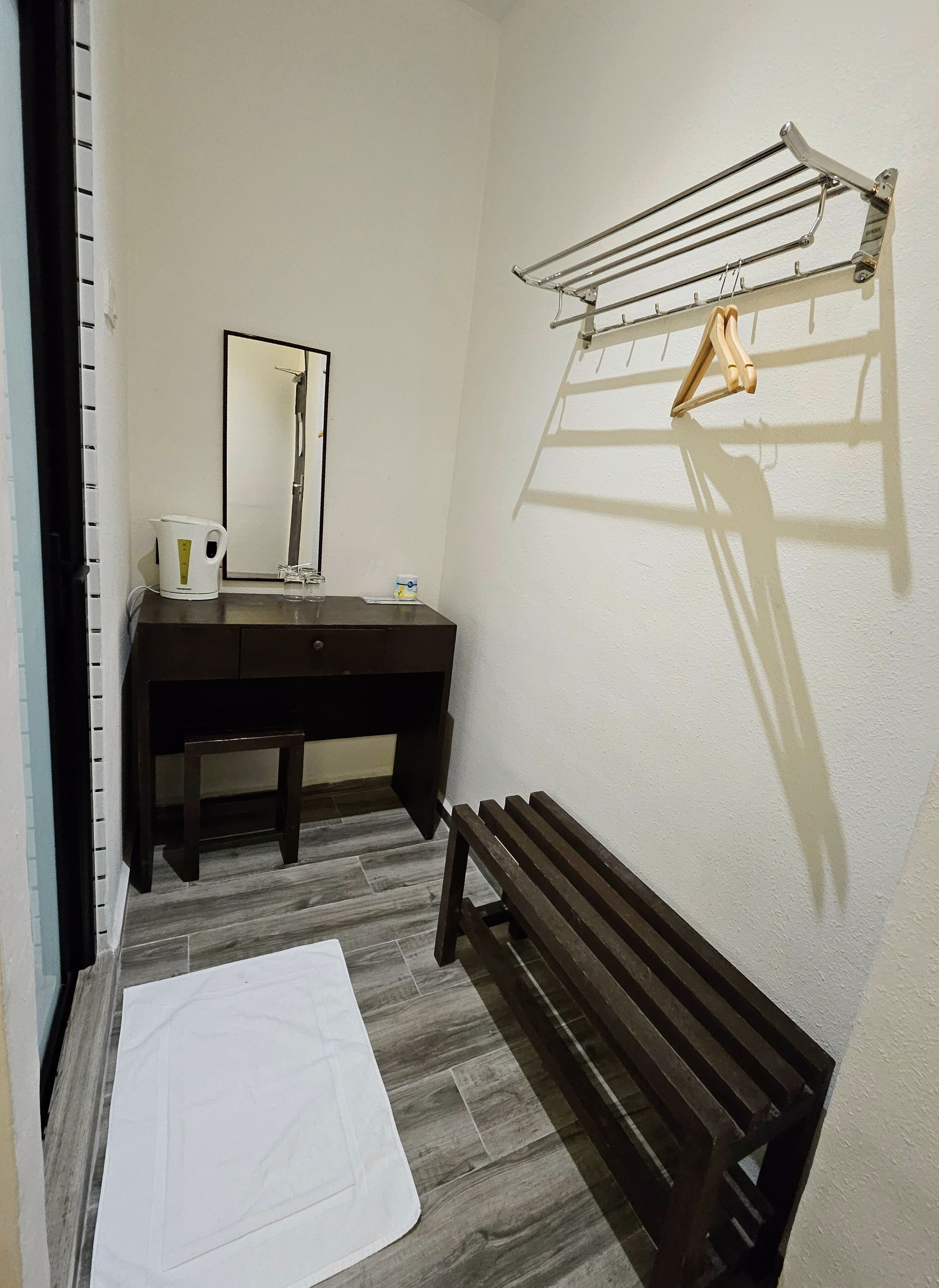 A bathroom with a dark wooden vanity, a mirror, a towel rack, and a bench.