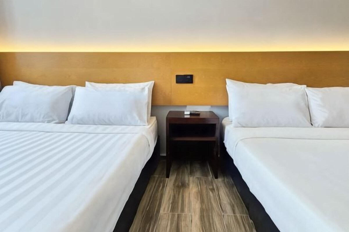 A hotel room with two beds, a nightstand, and a wall-mounted light fixture.