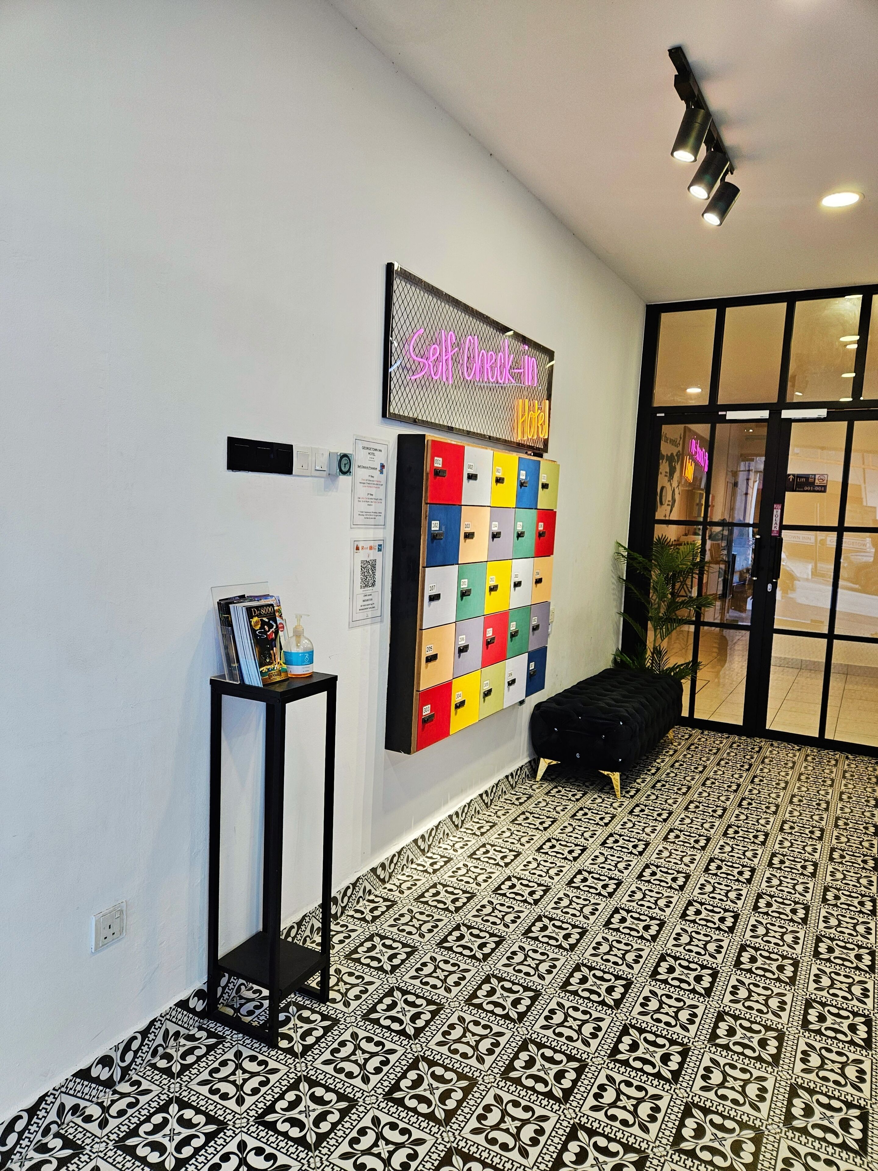 Um saguão de hotel com sistema de check-in automático, um mural de avisos e piso estampado.