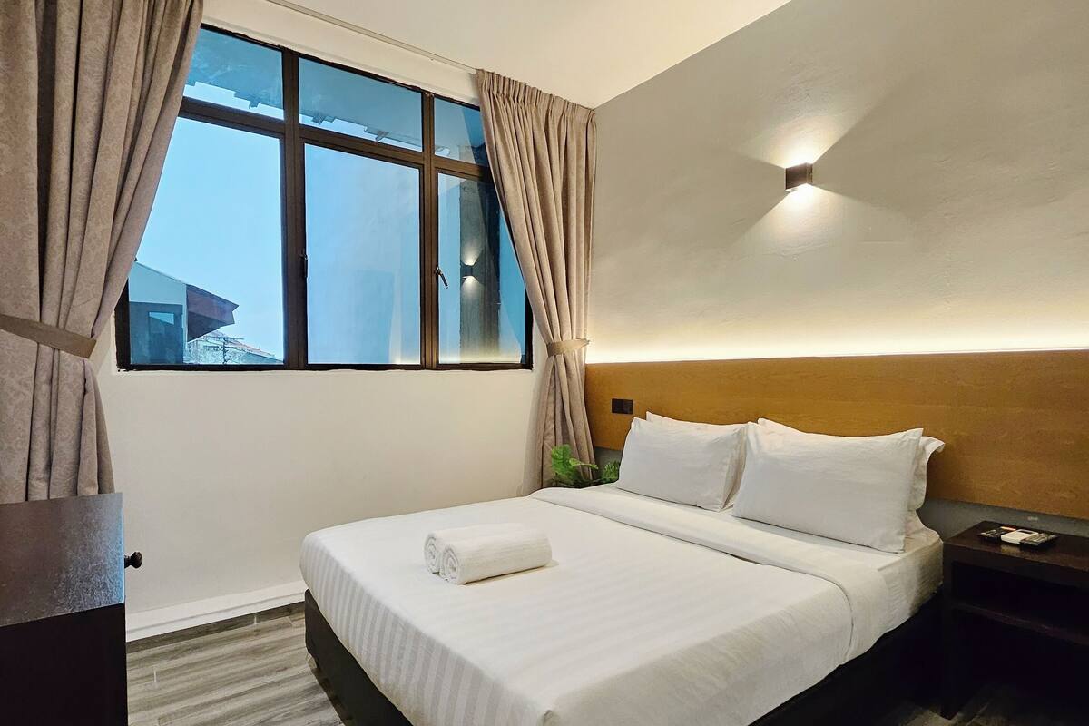Ein Hotelzimmer mit einem großen Bett, einem Nachttisch, einem Fenster mit Vorhängen und einer Deckenleuchte.