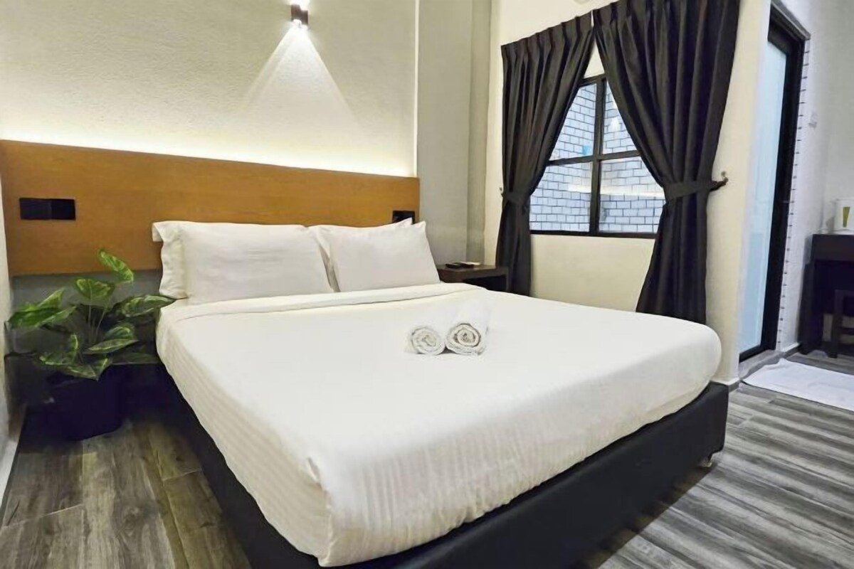 A neatly made bed with pillows and a blanket, a bedside plant, and a window with curtains.