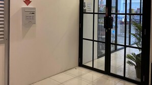 Une entrée d’hôtel moderne avec une boîte de dépôt pour les cartes de départ sans assistance, une porte en verre et une vue sur l’extérieur.