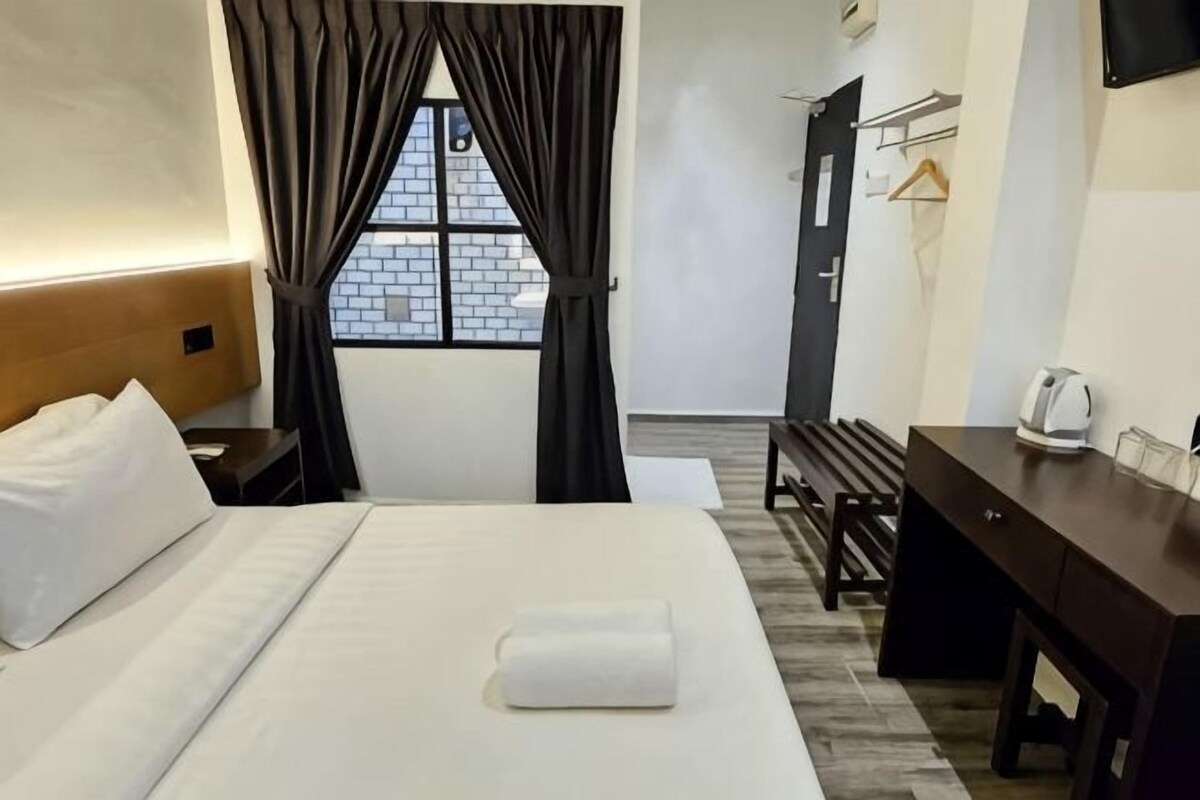 A hotel room with a bed, a desk, a chair, a window with curtains, and a view of the outside.