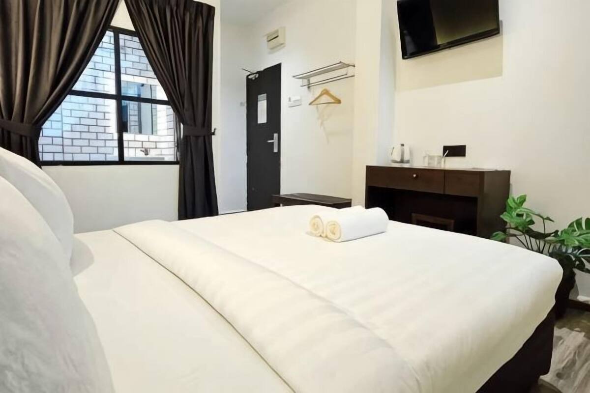 Ein Hotelzimmer mit Bett, Fernseher, Schreibtisch, Stuhl, Pflanze und einem Fenster mit Vorhängen.