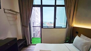 Une chambre d’hôtel avec un grand lit, un petit bureau et une vue sur un immeuble et un espace vert à l’extérieur.