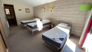 Une chambre avec trois lits simples, un mur en bois et une petite table.