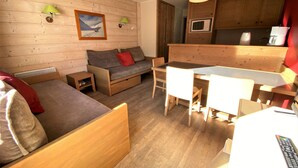 Une pièce chaleureuse avec un plancher en bois, un canapé, une petite table, une chaise et un coin cuisine équipé d’un four à micro-ondes et d’une bouilloire.