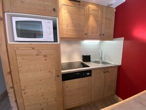 A compact kitchen with wooden cabinets, a microwave, a dishwasher, and a sink.
