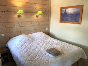 A bed with a quilted white duvet, two wall-mounted lamps, and a framed picture on the wall. - Family Duplex Ski-in/Ski-out, 6-7 pers (La Tania)
