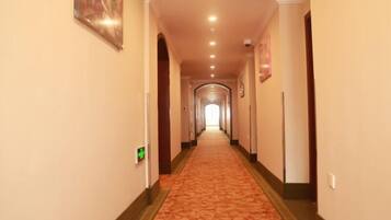 A hotel hallway with a carpeted floor, a light-colored wall, and a ceiling with recessed lighting.