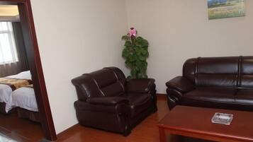 A hotel room with a bed, a brown leather sofa, a wooden coffee table, and a potted plant.
