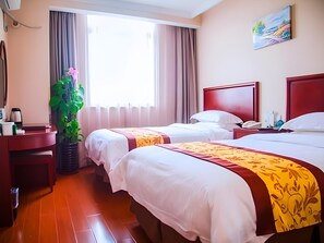 A hotel room with two beds, a desk, a plant, and a painting on the wall.