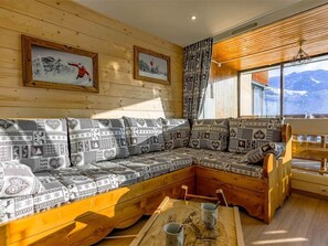 Interior acolhedor de uma cabana com um banco de madeira, área de estar com almofadas e quadros nas paredes.