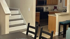 A dining area with a chandelier, wooden staircase, and a kitchen in the background. - 4 BR Home in Prestigious Regal Palms Resort, waterpark, close to theme parks. (Davenport)