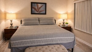 A neatly made bed with a patterned bedspread, two bedside tables with lamps, a framed artwork above the bed, and a window with blinds. - 4 BR Home in Prestigious Regal Palms Resort, waterpark, close to theme parks. (Davenport)