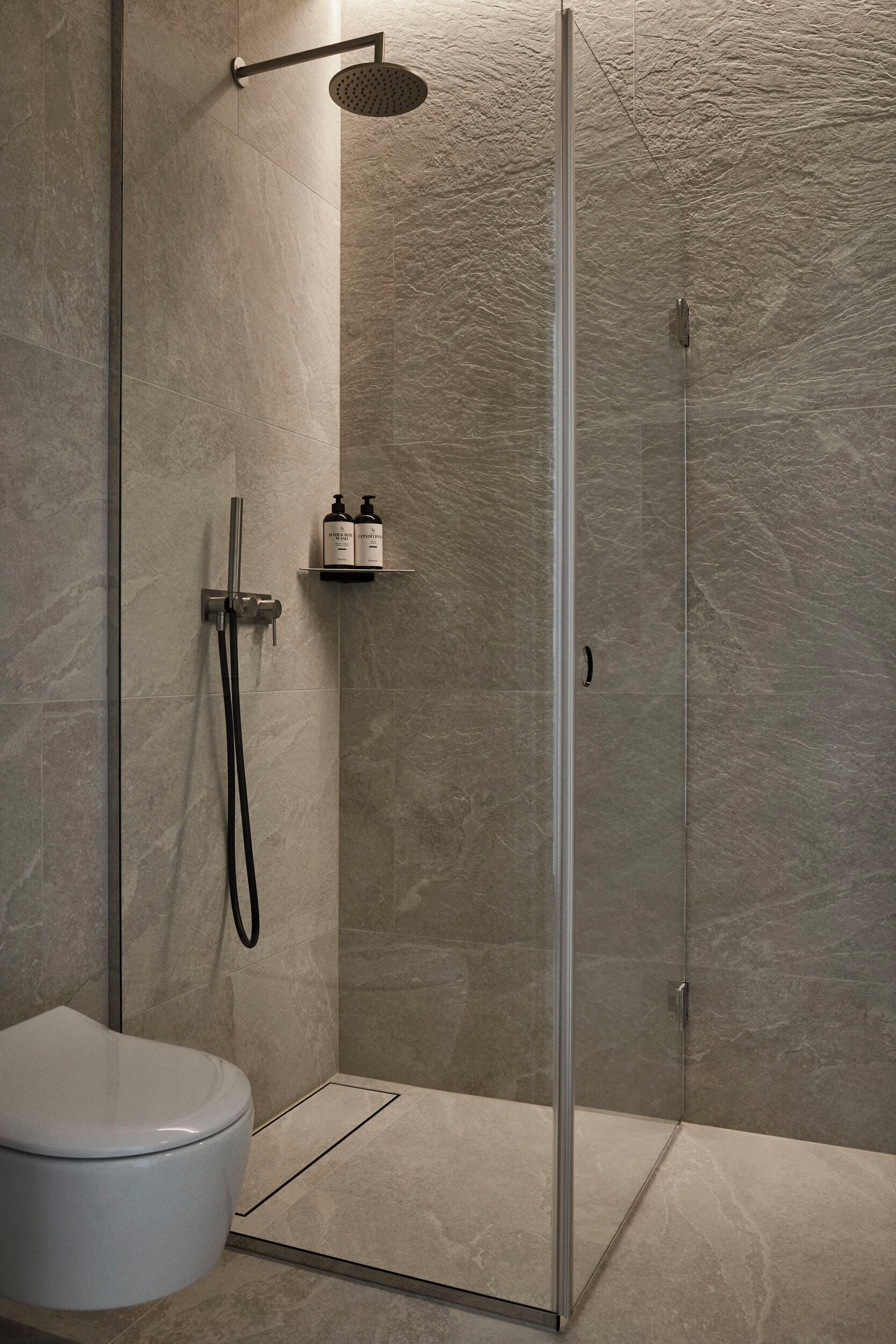 A modern bathroom with a glass-enclosed shower, a toilet, and a shelf with toiletries.