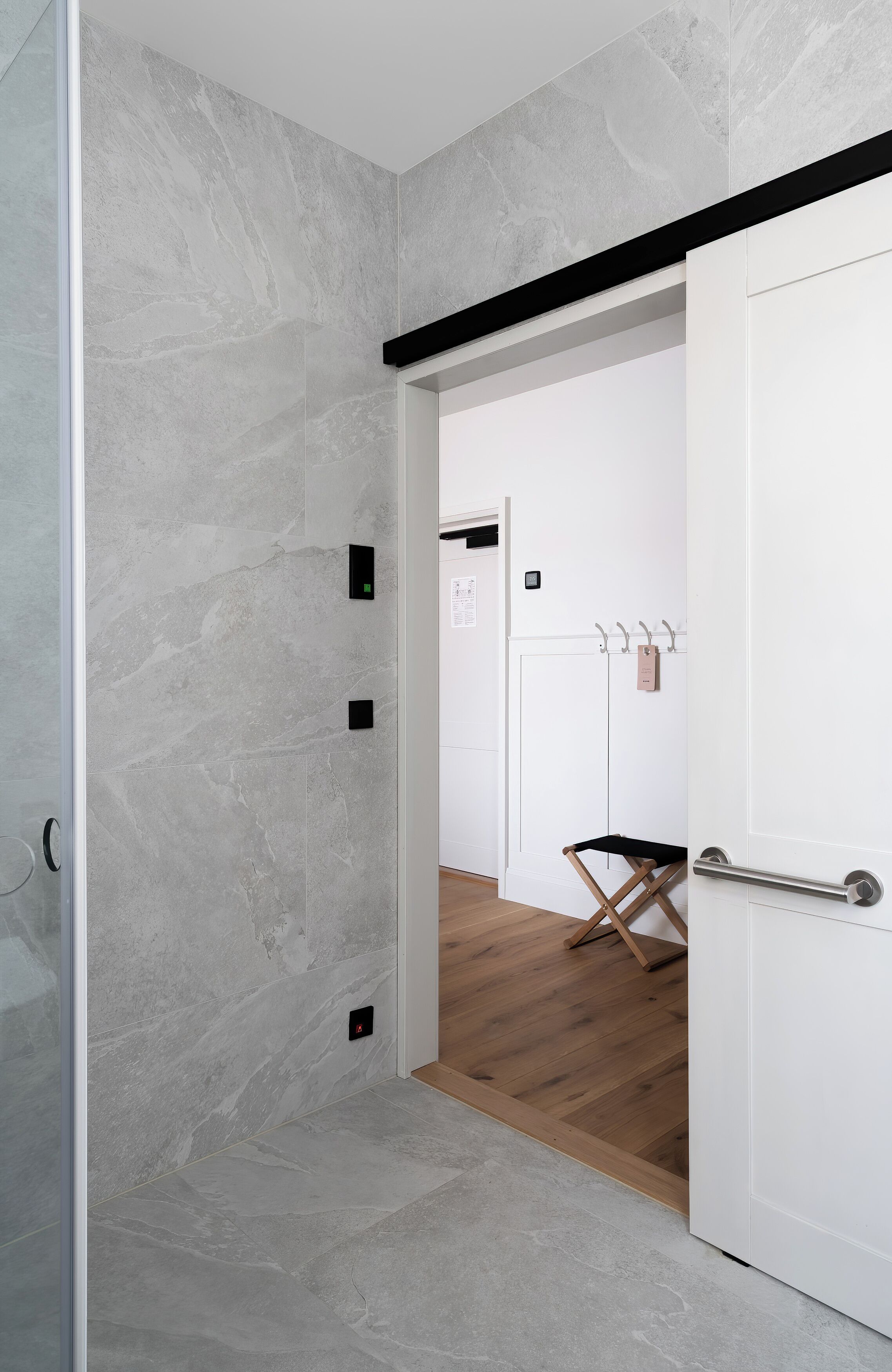 A hallway with a stone wall, a wooden floor, a white door, and a coat rack with a bag.
