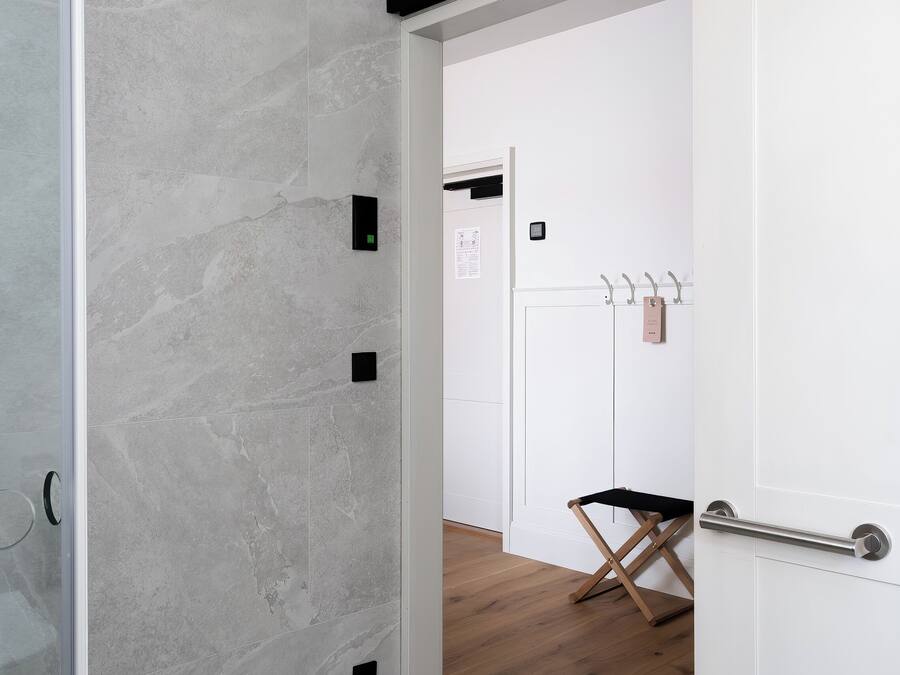 A hallway with a stone wall, a wooden floor, a white door, and a coat rack with a bag.