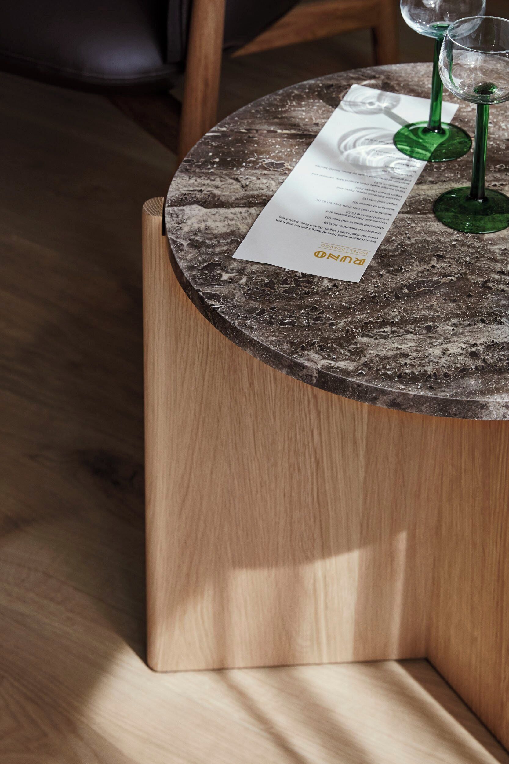 A round wooden table with a marble-like top, two green wine glasses, and a menu.