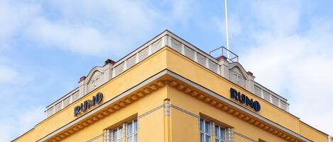 A building with the name 'RUNO' on its facade, featuring a yellow exterior and decorative window frames.