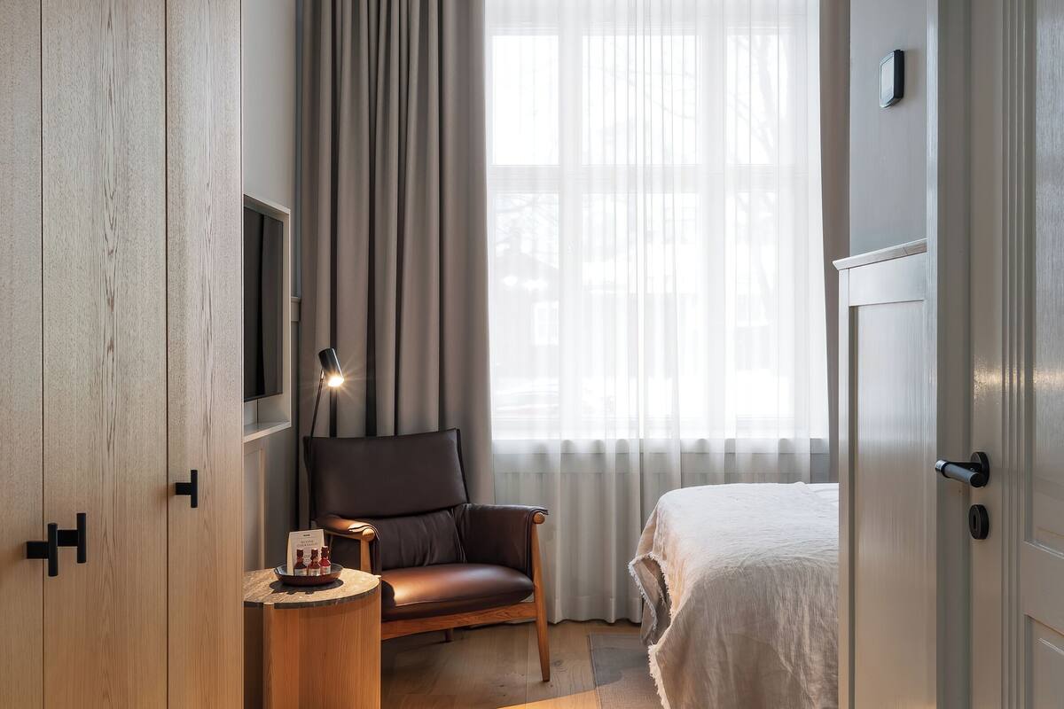 A hotel room with a bed, a desk with a lamp, a chair, and a TV mounted on the wall.