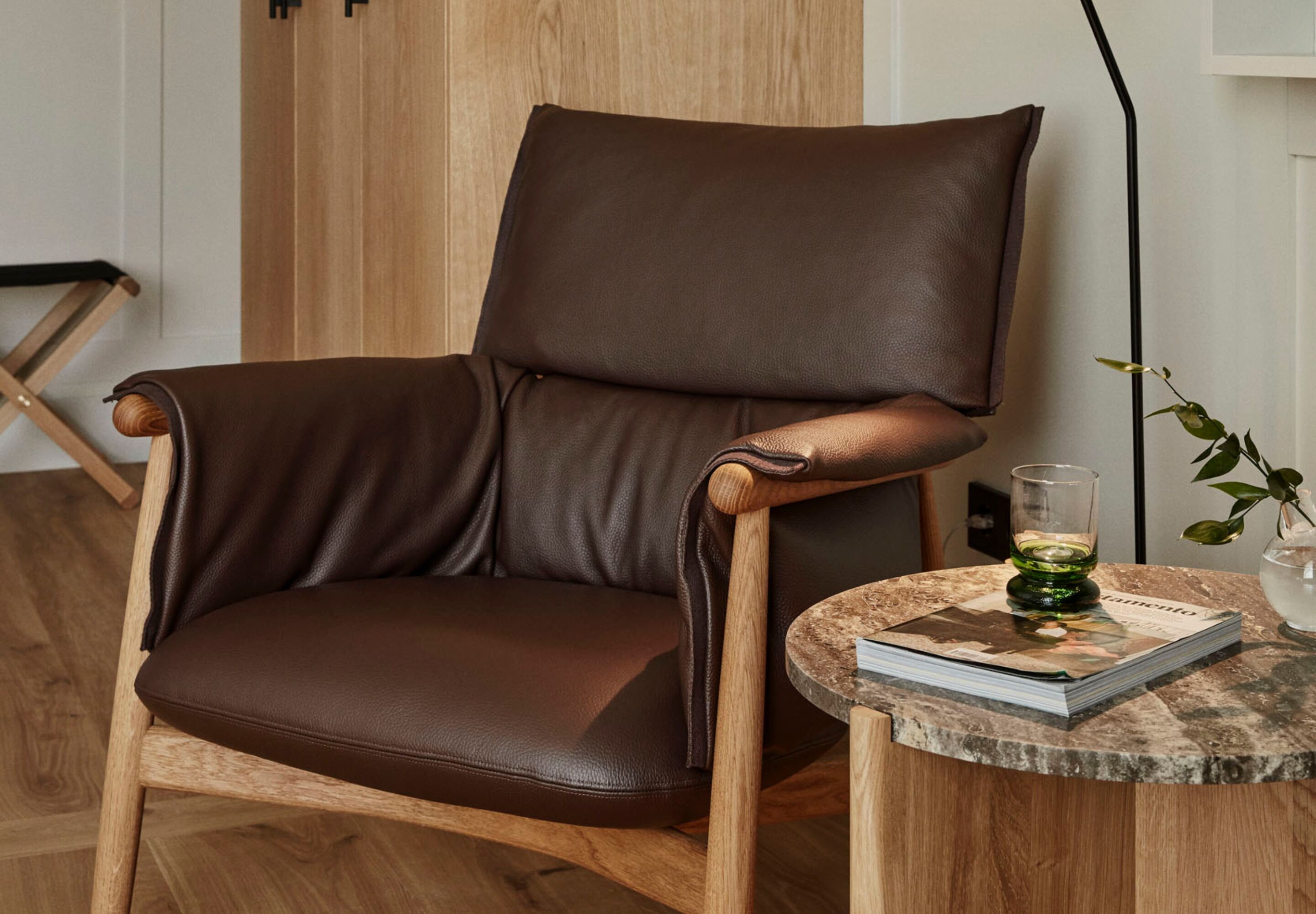 Un sillón de cuero marrón con reposabrazos de madera y suelo de madera.