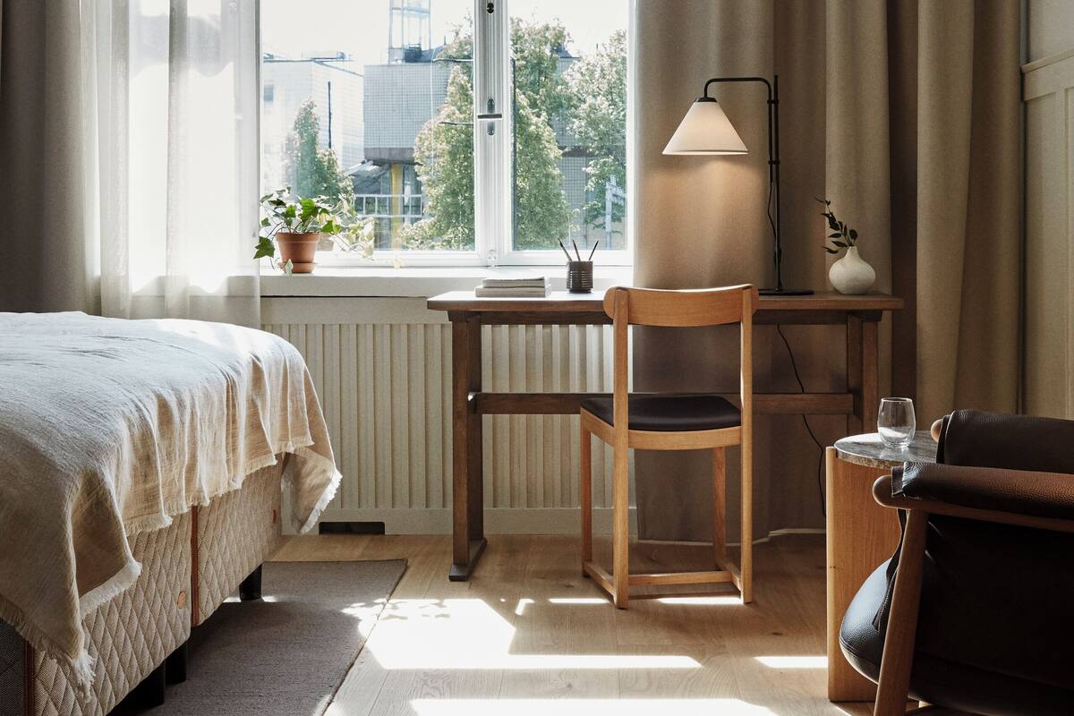 A bedroom with a bed, a desk, a chair, a lamp, and a view of the outside.