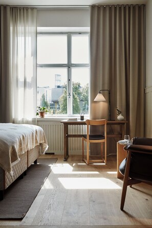 A bedroom with a bed, a desk, a chair, a lamp, and a view of the outside.