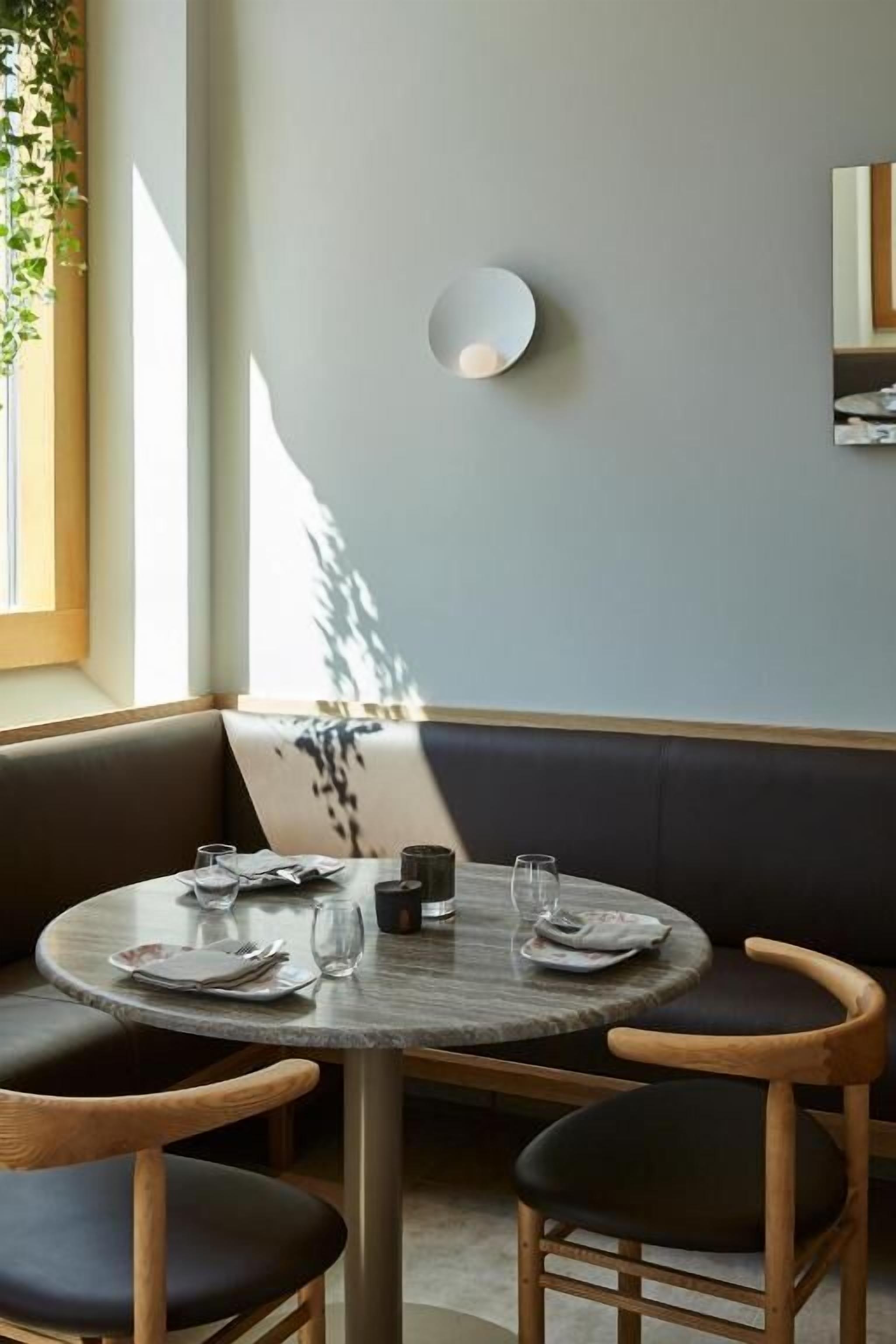 En spiseplads med et rundt bord, to stole, en bænk og en vægmonteret lampe.