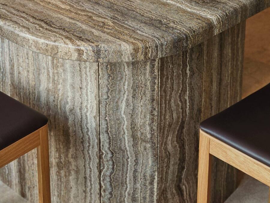 A marble-topped table with a curved edge, accompanied by two wooden chairs with dark cushions.