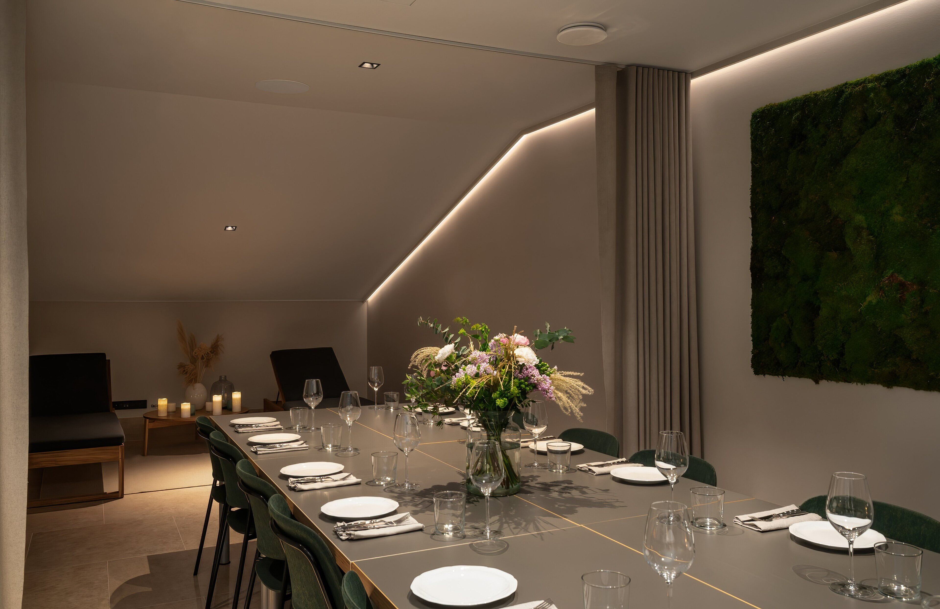 A modern dining room with a long table set for six, a vase of flowers, and a green wall art piece.