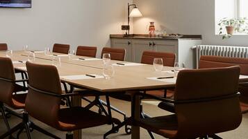 A conference room with a long table, brown chairs, a lamp, and a radiator.