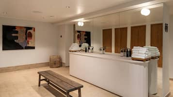 Relax in a serene bathroom with a large mirror, a comfortable bench, and a stylish counter with towels and toiletries.